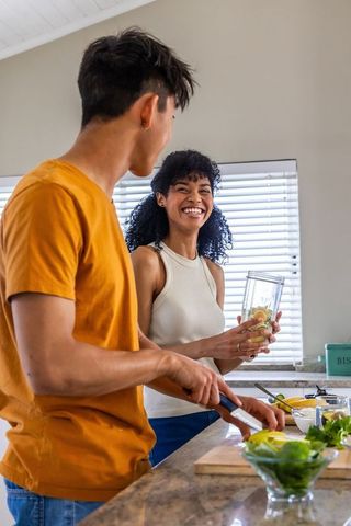 Diverse couple preparing fresh citrus smoothie in bright modern kitchen