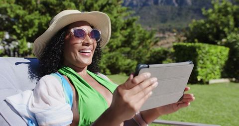 Smiling african american woman relaxing on lounge with tablet in sunny backyard