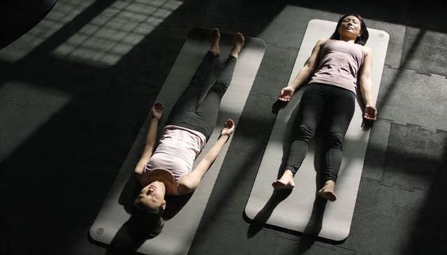 Two asian women practicing restorative yoga lying on mats with dramatic grid shadows