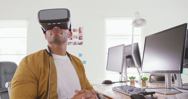 A young professional is using a VR headset at a modern workstation with multiple computer screens. Ideal for use in contexts related to technology, innovation, modern workplaces, and virtual reality applications in professional environments.