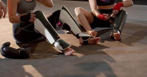 Three training partners fastening shin guards and hand wraps before sparring session