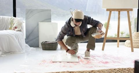 Indian male artist crouching applying paint on canvas in bright minimalist studio