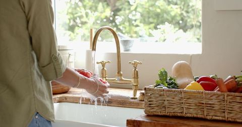 Woman washing tomatoes under brass faucet in rustic kitchen