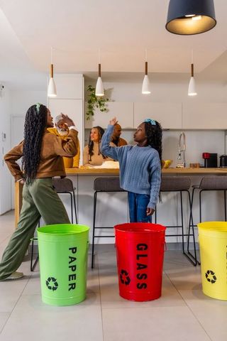 Family teaching kids recycling at kitchen island with colorful paper glass plastic bins