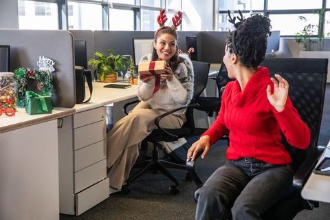 Diverse coworkers exchanging holiday gifts in open-plan office wearing reindeer headbands