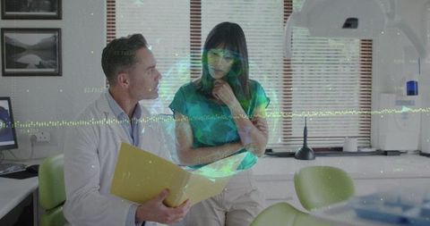 Doctor consulting patient in dental clinic while reviewing files with digital data overlay