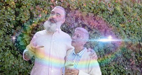 Mature couple enjoying morning coffee by garden hedge with rainbow light flare