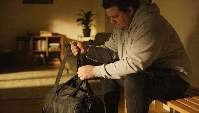 Man packing black duffel bag on wooden bench in cozy living room with warm golden light