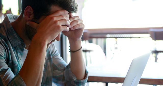 Stressed Man Holding Head While Working on Laptop in Cafe - Download Free Stock Images Pikwizard.com