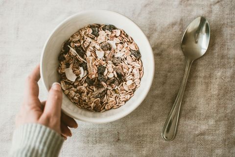 Hand Holding Bowl of Muesli with Dried Fruit and Coconut Flakes on Linen Table
