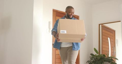 African man carrying cardboard box through home entryway smiling