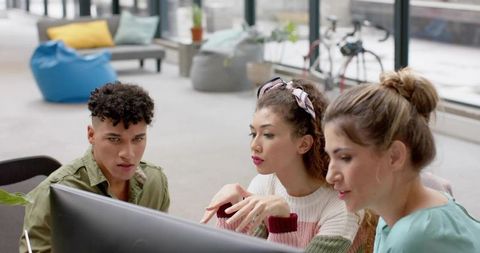 Young team collaborating around monitor in bright coworking lounge