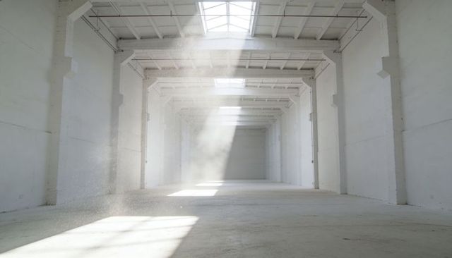 Sunlit empty industrial warehouse featuring skylight dust beams and concrete interior