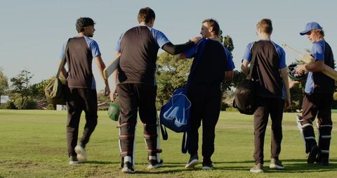 Walking diverse male cricket teammates carrying bats and bags celebrating teamwork