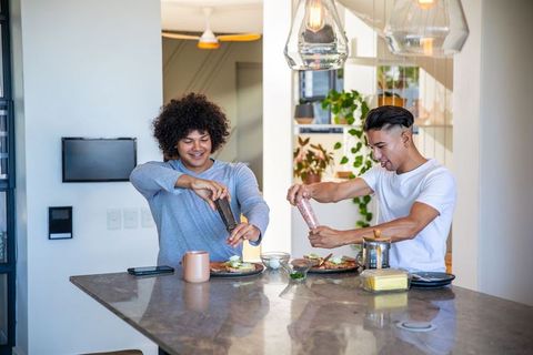 Young Friends Laughing Over Bread and Avocado Meal in Modern Kitchen