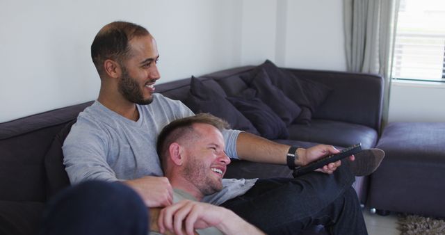 Multi ethnic gay male couple sitting on couch and watching tv - Download Free Stock Photos Pikwizard.com