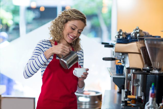 Smiling waitress making cup of coffee at counter in cafe