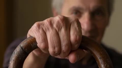 Senior man gripping worn wooden cane close-up, conveying steadying strength and vulnerability