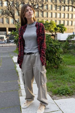 Young woman standing on sidewalk wearing red plaid shirt and cargo pants street style