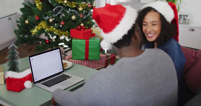 Couple Wearing Santa Hats Celebrating Christmas with Laptop by Christmas Tree - Download Free Stock Images Pikwizard.com