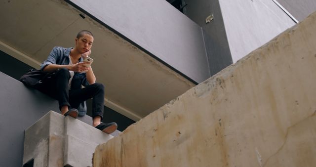 Young Man Sitting Outdoor on Building Ledge Checking Smartphone - Download Free Stock Images Pikwizard.com