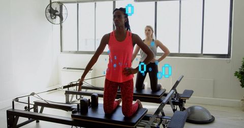 Kneeling women on reformer holding straps practicing Pilates workout in sunlit studio