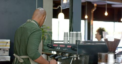 African american barista operating espresso machine in bright modern coffeehouse