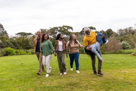 Multigenerational african american family walking and playing in park on overcast day