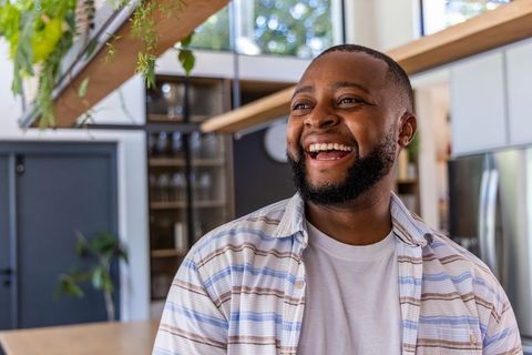Laughing african man in bright modern kitchen with hanging plants and striped shirt