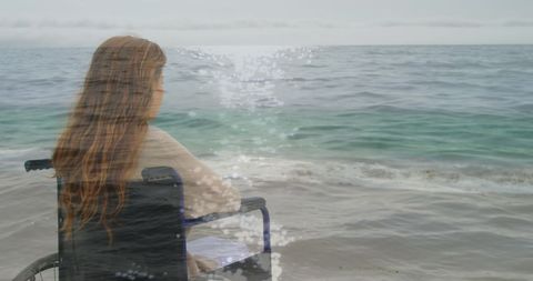 Woman in wheelchair overlooks peaceful sea in reflective scene