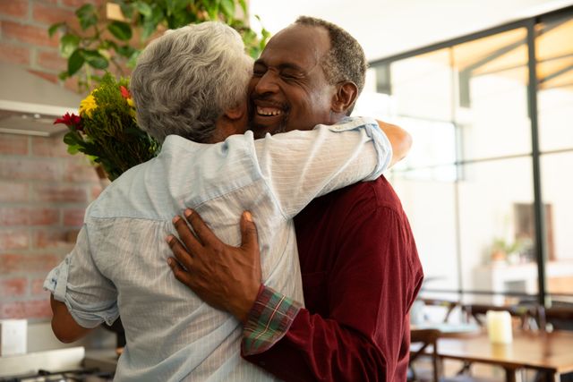 Senior African American couple hugging and smiling at home, showing affection and happiness. Ideal for use in articles or advertisements about elderly relationships, love, and togetherness during quarantine or self-isolation periods. Can also be used in content related to Covid-19, social distancing, and maintaining emotional connections.