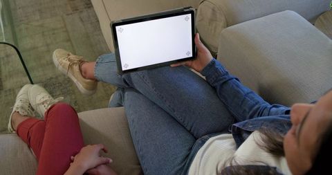 Adult holding tablet with blank vertical screen on lap while relaxing on sofa with child