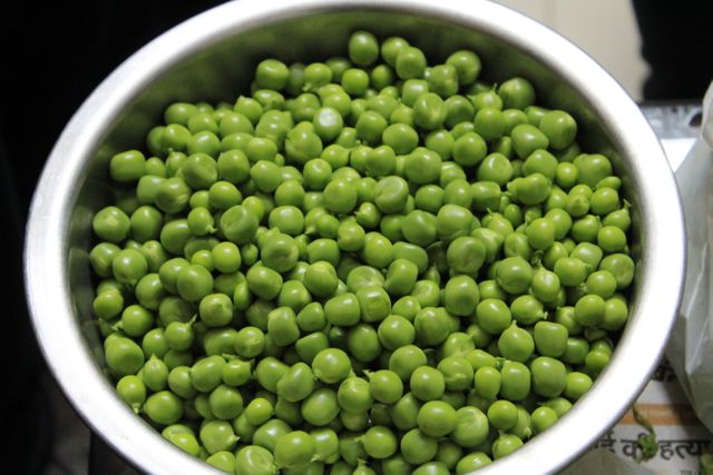 Fresh green peas in a stainless steel bowl, ideal for illustrating concepts of organic produce, healthy eating, and natural ingredients. Suitable for use in cooking blogs, recipe websites, and health food promotions.