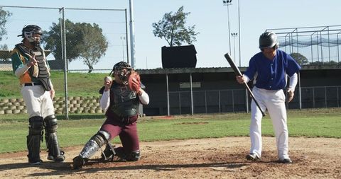 Mature baseball catcher ready behind batting opponent on sunny field