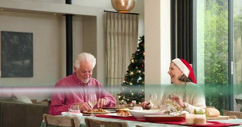 Seniors sharing christmas dinner, man in pink shirt and woman wearing santa hat, smiling