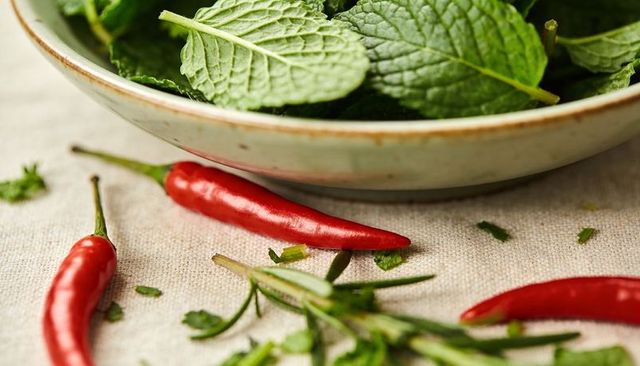 Glazed bowl holding fresh mint with red chilies and rosemary on rustic linen closeup food