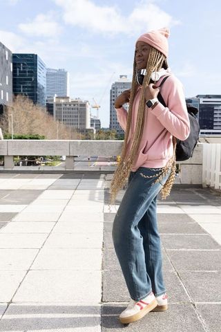 Young african american woman standing on urban terrace wearing pink hoodie and backpack