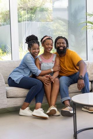 Smiling african american family hugging teen daughter on sunlit living room sofa