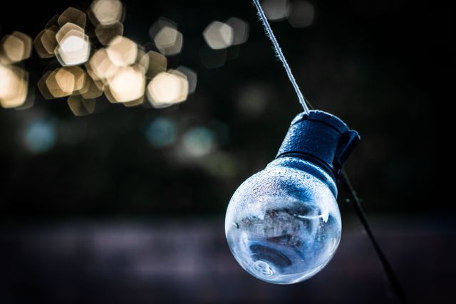 Outdoor string light hanging against a backdrop with bokeh effect. Suitable for festive, holiday, or party themes. Ideal for use in graphics related to decoration, evening events, and backyard or garden lighting.