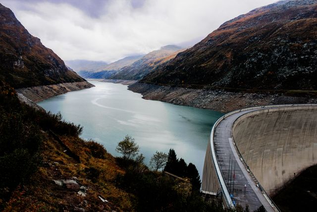 Reservoir in mountainous region with dam and overcast sky. Suitable for environmental studies, travel promotions, landscape appreciation, and presentations on water management.