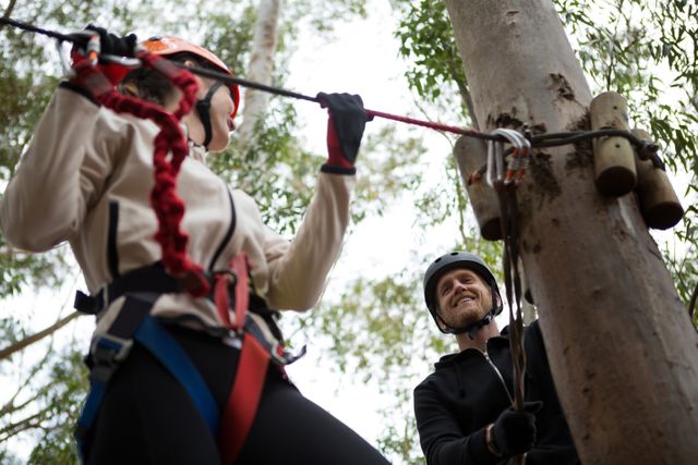 Woman holding zip line in forest, wearing safety gear and helmet. Ideal for promoting outdoor activities, adventure sports, team-building events, and nature exploration. Suitable for use in travel brochures, adventure tour websites, and outdoor gear advertisements.