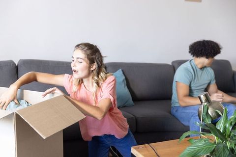 Young couple unpacking cardboard box in modern living room during moving day