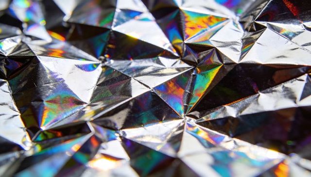 Holographic metallic foil folding into faceted iridescent texture with rainbow highlights