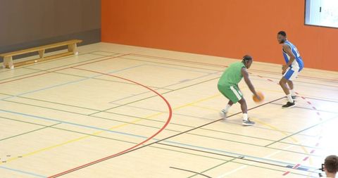 Defender pressuring ball handler dribbling crossover on indoor gym basketball court