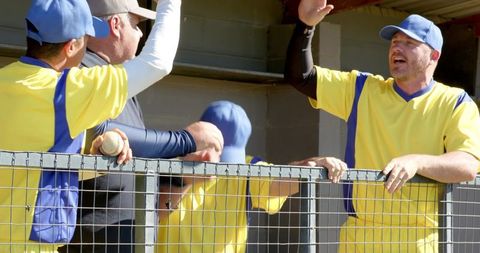 Semi-pro baseball team cheering in dugout wearing yellow jerseys and blue caps