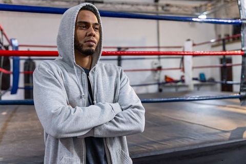 Focused athlete in hooded sweatshirt standing by boxing ring preparing for training