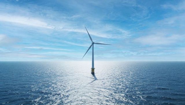 Offshore wind turbine rotating above endless sea with sunlit reflection and blue sky