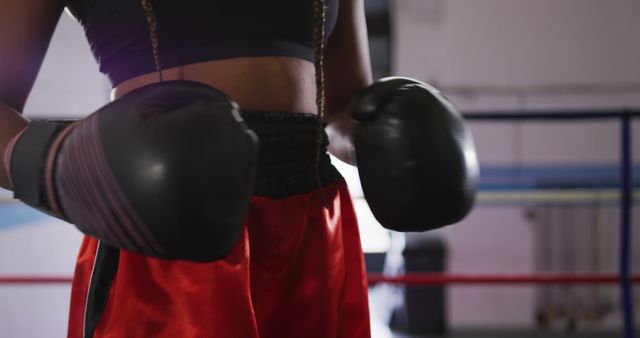 Female boxer wearing boxing gloves, preparing for training in a gym. Useful for content related to sports, fitness, boxing training, women's empowerment, and healthy lifestyles.