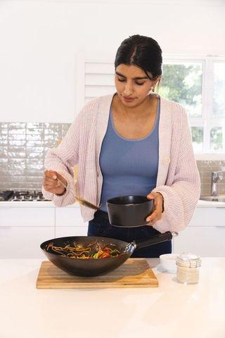 Woman Cooking Noodles and Vegetables in Modern Kitchen