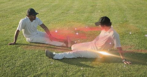 Two Cricketers Relaxing on Outfield Grass After Match Chatting in Warm Sunlight